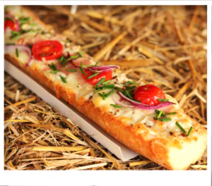 Close-up diagonal view of a cheese-topped baguette with cherry tomatoes and chives on hay.
