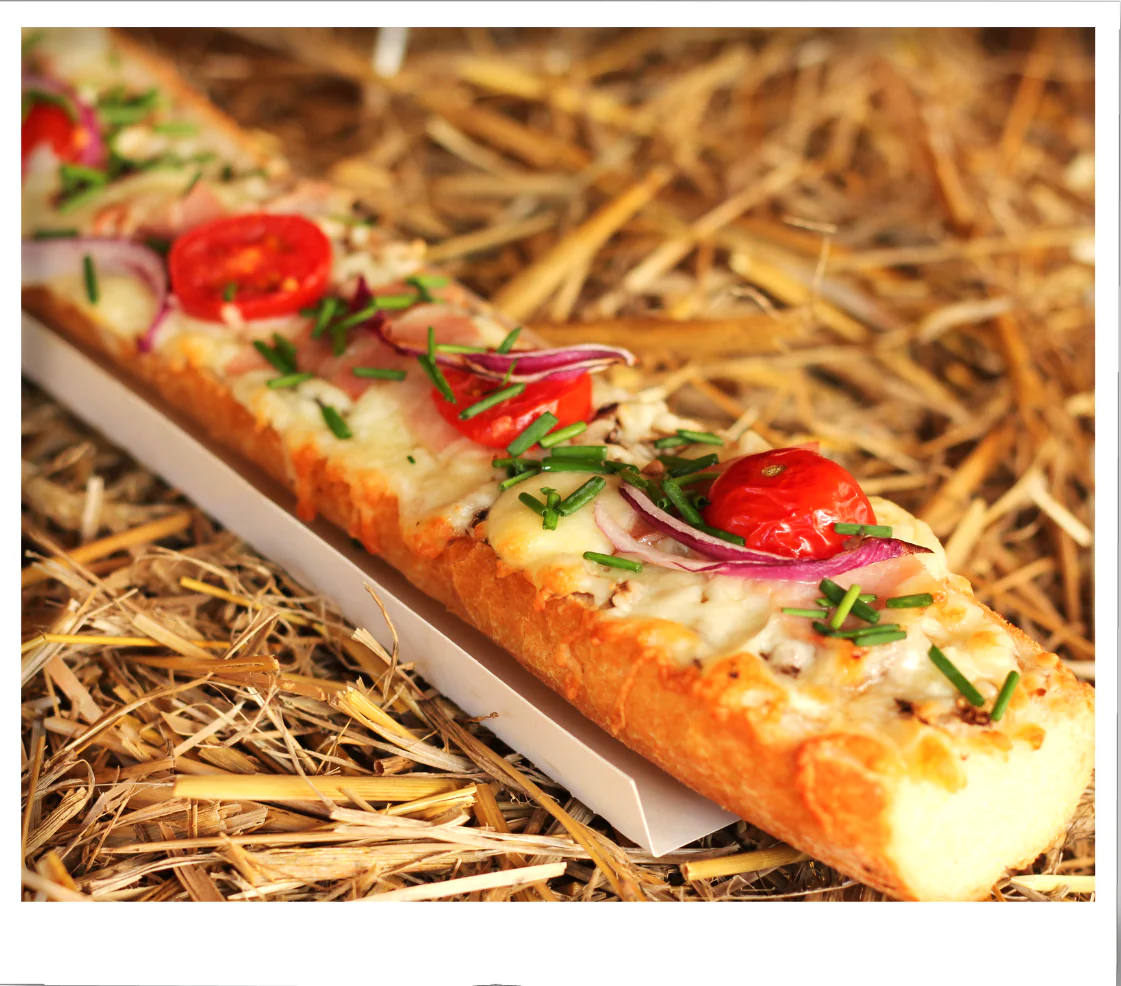 Toasted baguette topped with melted cheese, cherry tomatoes, red onion, and chives, displayed on straw.